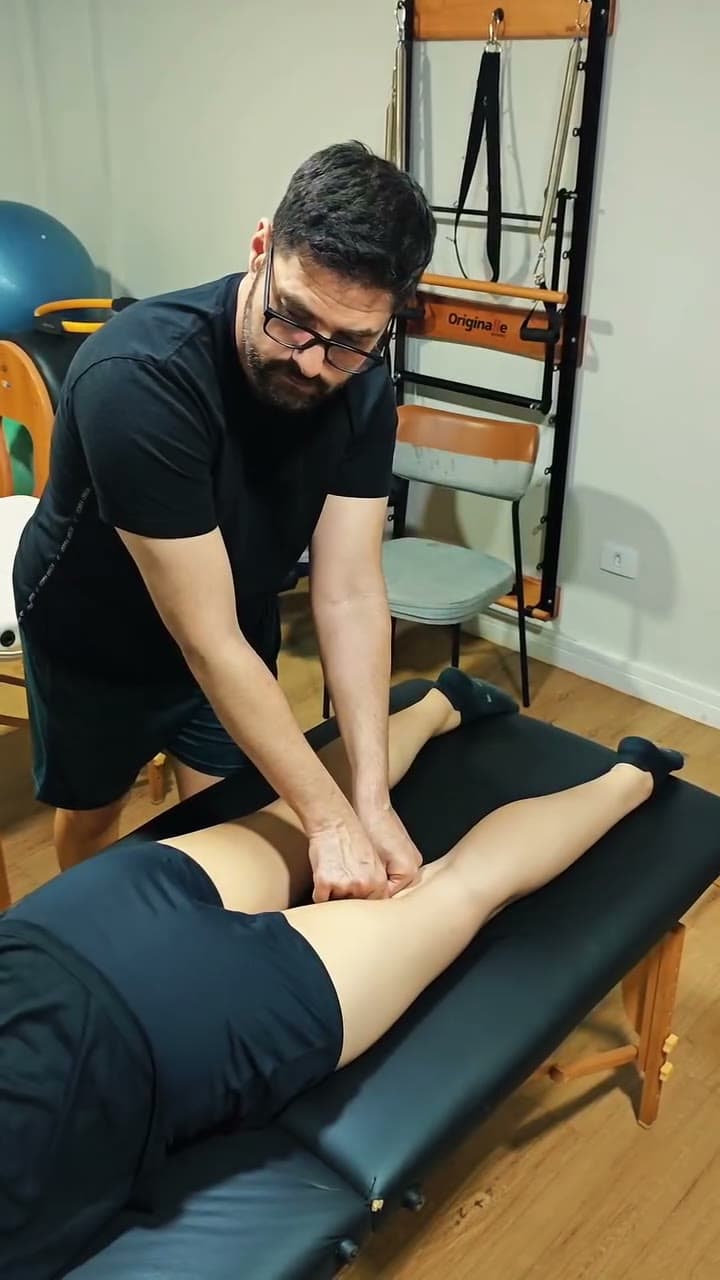 Fisioterapeuta da BioMoov fazendo terapia manual na perna de uma paciente deitada na maca, com aparelhos de Pilates ao fundo