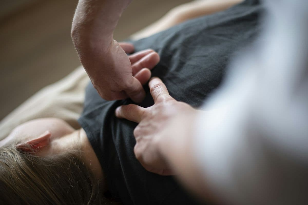 Mãos de terapeuta liberando a musculatura do ombro de um paciente deitado