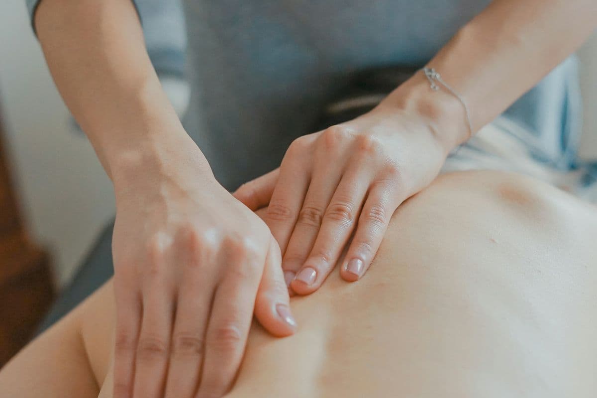 Mãos de massoterapeuta massageando as costas de uma pessoa