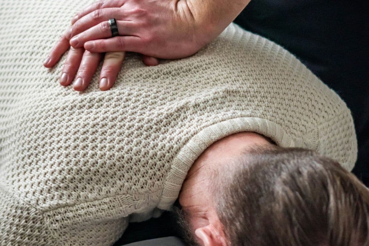 Mãos de terapeuta posicionadas nas costas de um paciente para manipulação